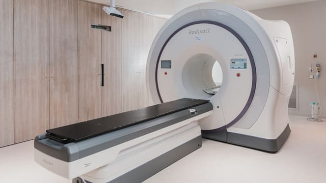 A white medical radiation therapy machine with a black patient table in a clinic
