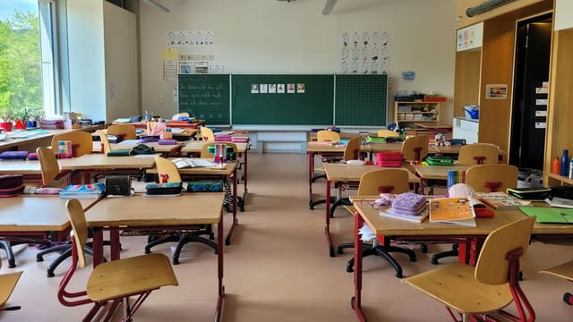Salle de classe vide avec tableau noir et pupitres en bois, avant l'installation d'un brasseur d'air au plafond.