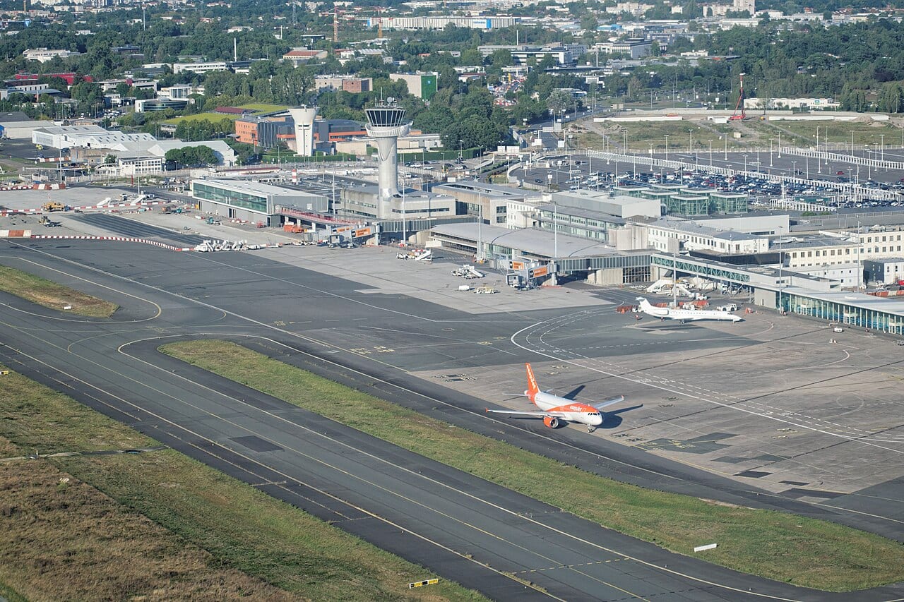 Vue aérienne de l'aéroport de Bordeaux-Mérignac, avec la tour de contrôle, les terminaux et un avion de ligne sur le tarmac.