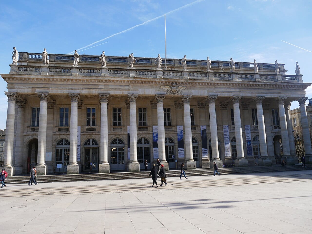 Façade à colonnes corinthiennes du Grand-Théâtre de Bordeaux, place de la Comédie, avec quelques passants devant les marches.