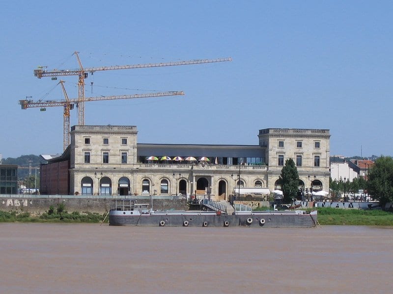 Vue de la rive droite de la Bastide à Bordeaux avec ses bâtiments en pierre et des grues de chantier en arrière-plan.