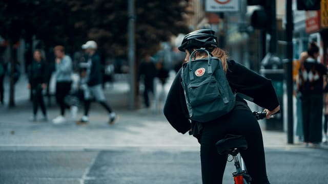 Personne en veste noire et pantalon noir avec sac vert à vélo en plein jour