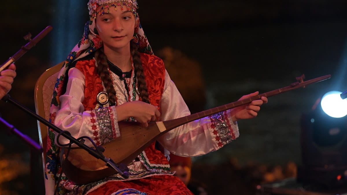 A woman in traditional dress plays an instrument.