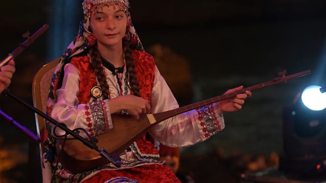 A woman in traditional dress plays an instrument.