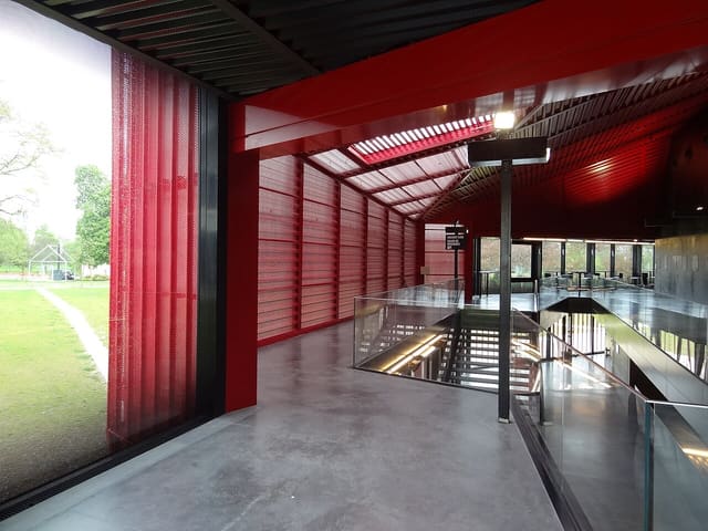 Hall du Rocher de Palmer, aux structures rouges et noires, avec un escalier vitré et le parc visible à travers la baie.