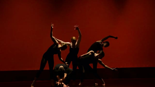 Quatre danseurs en silhouette sur fond rouge sombre, bras levés, dans des postures contrastées sur une scène.