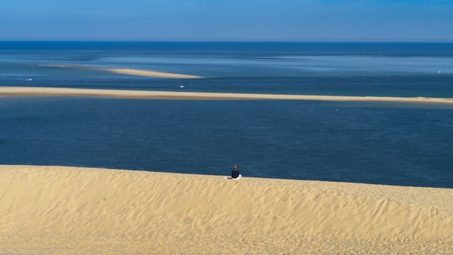 Silhouette d'une personne au sommet d'une dune de sable face à l'océan