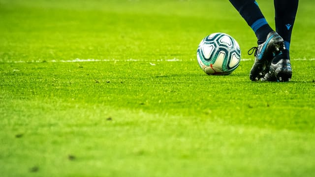 Gros plan sur un ballon de football et des crampons sur une pelouse.