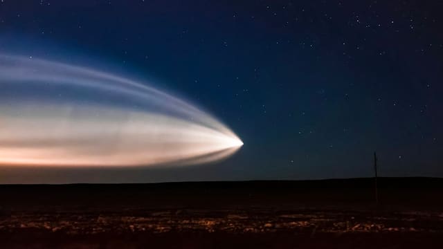 Traînée lumineuse d'une fusée dans un ciel étoilé au-dessus d'une plaine sombre