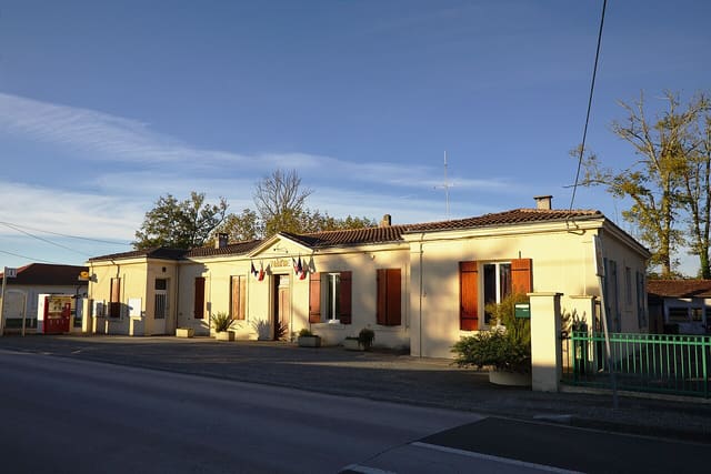 La mairie de Saumos, bâtiment de plain-pied à façade claire et volets bruns, sous un ciel bleu d'automne.