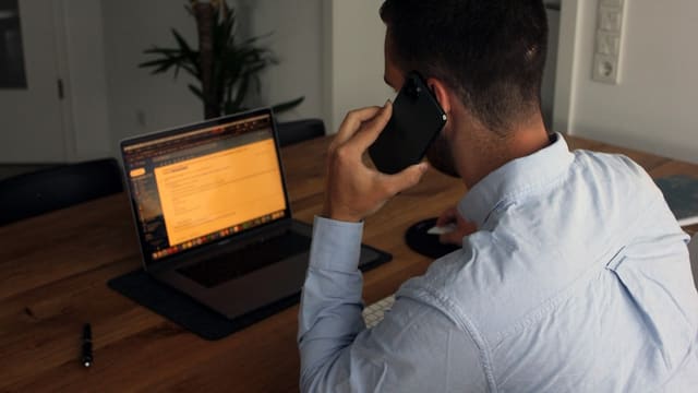 man in blue dress shirt holding black smartphone