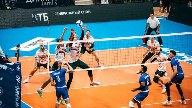 Joueurs de volley-ball de part et d'autre du filet, lors d'un contre à la volée dans une salle.