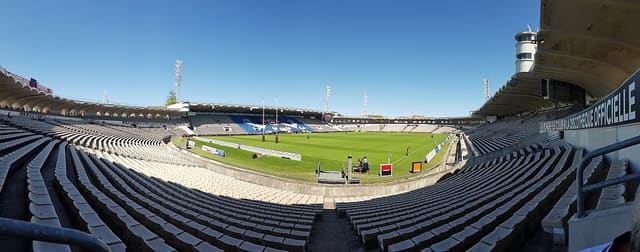 Vue panoramique des tribunes et de la pelouse du stade Chaban-Delmas à Bordeaux, sous un ciel bleu.