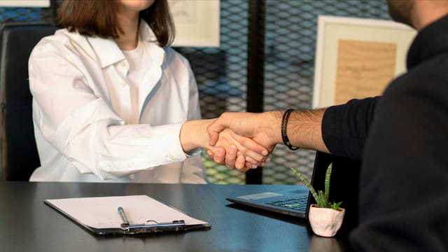 a man and a woman shaking hands in front of a laptop
