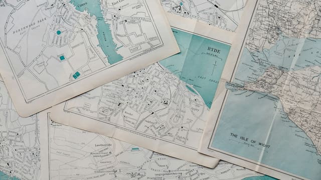Plusieurs cartes anciennes de villes posées les unes sur les autres, illustrant la consultation sur le plan local d'urbanisme.