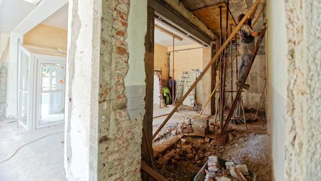 Chantier de rénovation dans un logement : murs de brique éventrés, gravats et ouvrier sur une échelle