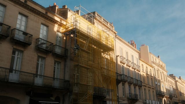 Façades en pierre blonde d'un immeuble bordelais, dont l'une est couverte d'un échafaudage, sous un ciel bleu.
