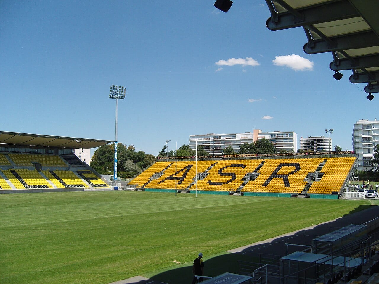 Tribune jaune et noire du stade Marcel-Deflandre à La Rochelle, aux sièges dessinant les lettres ASR, devant la pelouse vide.